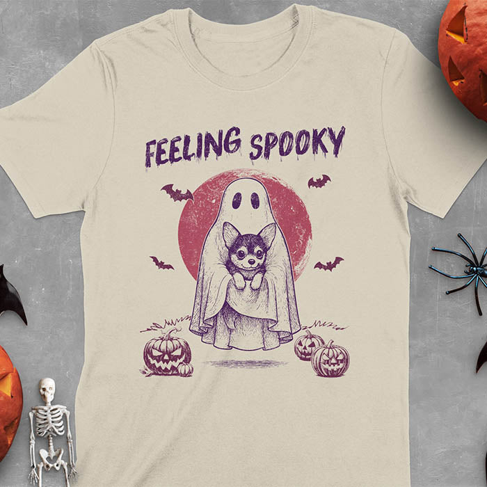 Sand color t-shirt featuring a ghost holding a corgi puppy with 'Feeling Spooky' text above, red moon background with bats and jack-o'-lanterns