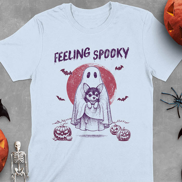 Light blue t-shirt featuring a ghost holding a corgi puppy with 'Feeling Spooky' text above, red moon background with bats and jack-o'-lanterns