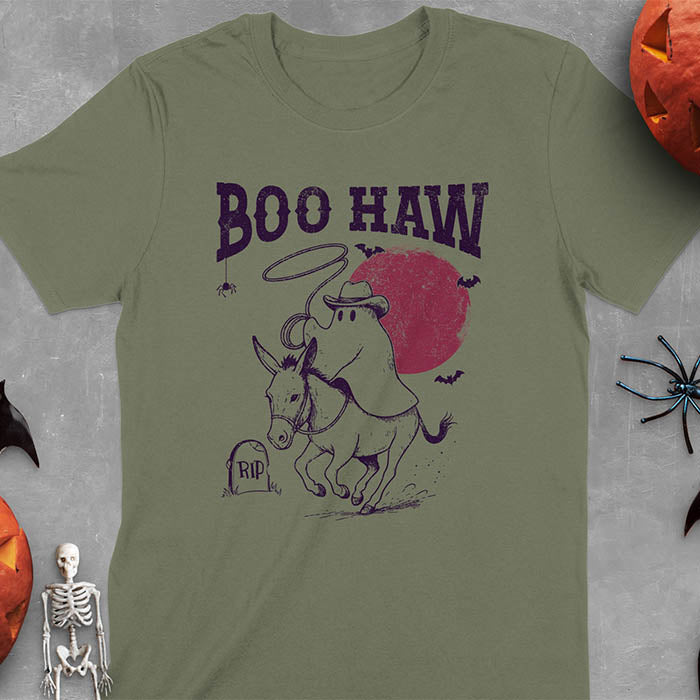 Military Green t-shirt featuring cowboy ghost riding a donkey with lasso, 'BOO HAW' text above, red moon background with bats and RIP tombstone