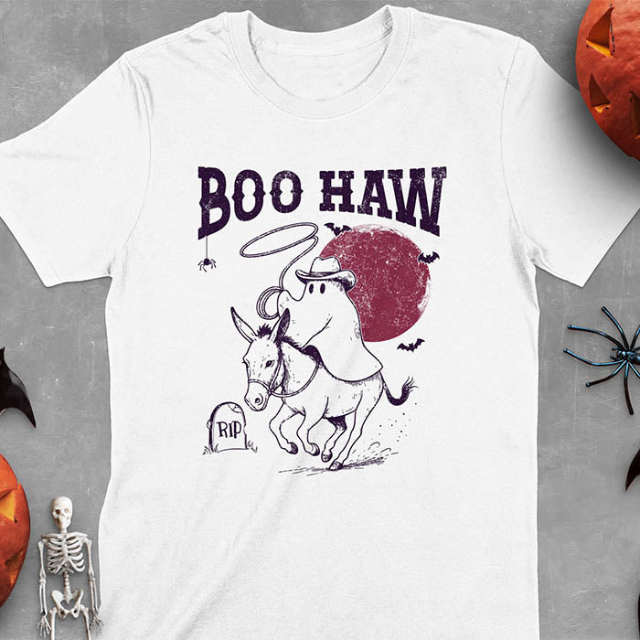 White t-shirt featuring cowboy ghost riding a donkey with lasso, 'BOO HAW' text above, red moon background with bats and RIP tombstone