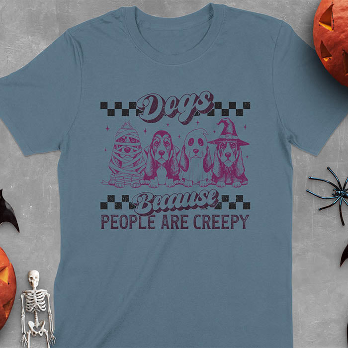 Indigo Blue t-shirt featuring four basset hounds in Halloween costumes - mummy, ghost, witch, and vampire - with 'Dogs Because People Are Creepy' text and checkered borders