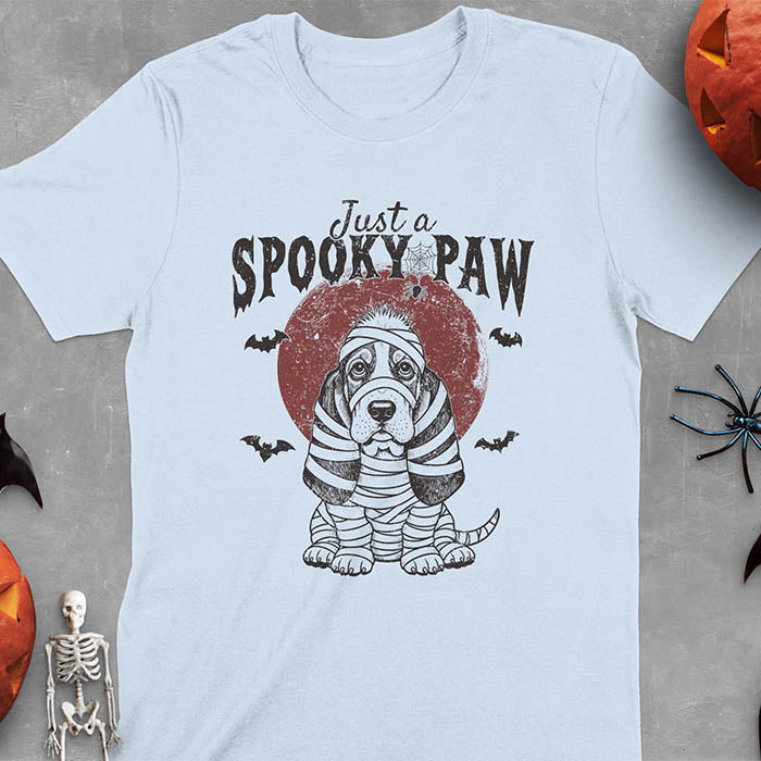 Light blue t-shirt featuring a cute basset hound wrapped in white mummy bandages with 'Just a SPOOKY PAW' text above