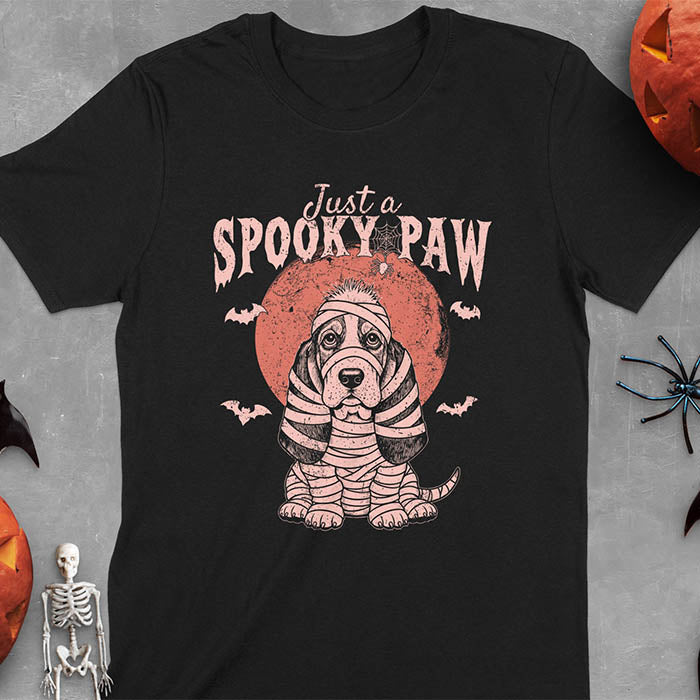 Black t-shirt featuring cute a basset hound wrapped in white mummy bandages with 'Just a SPOOKY PAW' text above