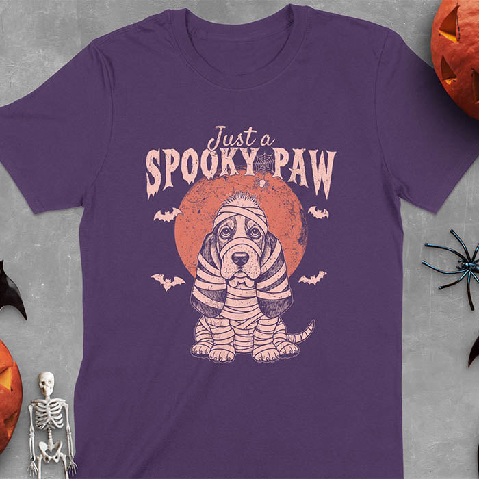 Purple t-shirt featuring a cute basset hound wrapped in white mummy bandages with 'Just a SPOOKY PAW' text above