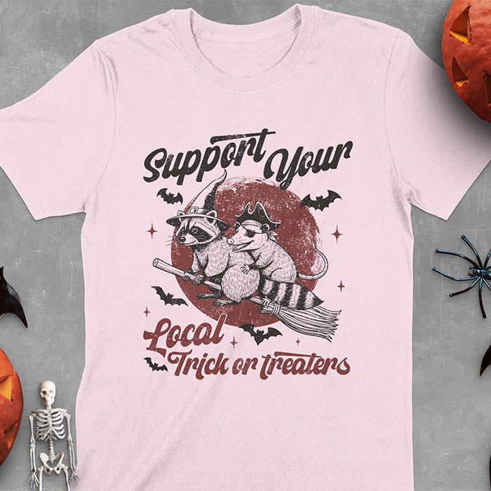 Light Pink t-shirt Halloween witch raccoon design featuring opossum pirate on broom with Support Your Local Trick or Treaters text