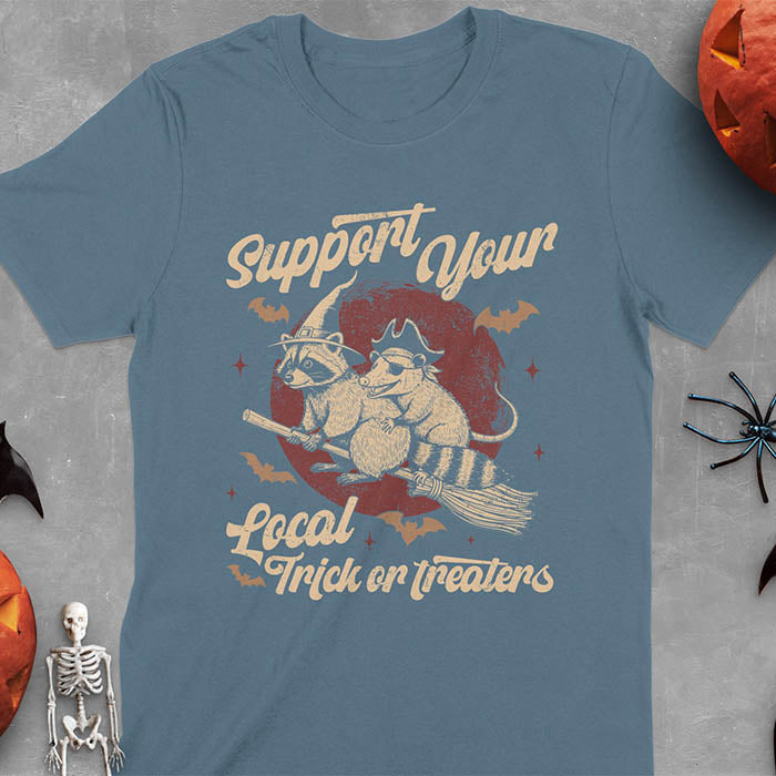 Indigo Blue t-shirt Halloween witch raccoon design featuring opossum pirate on broom with Support Your Local Trick or Treaters text