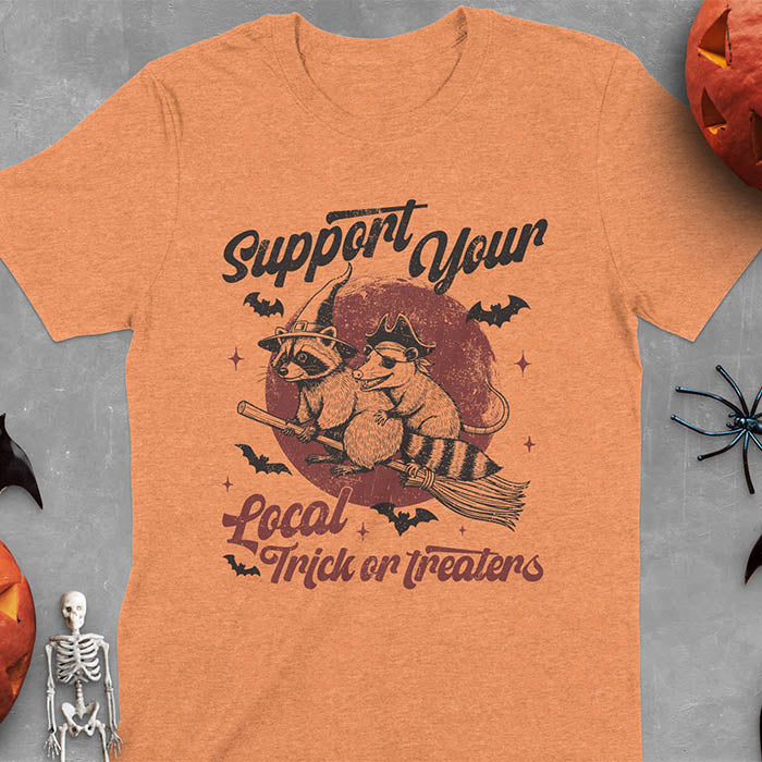 Heather Orange t-shirt Halloween witch raccoon design featuring opossum pirate on broom with Support Your Local Trick or Treaters text