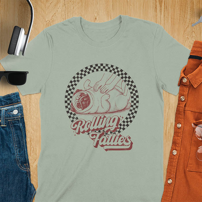 Sage green t-shirt with 'Rolling Fatties' text and illustration of chubby pug lying on its back inside black and white checkered circle border, with human hands reaching toward pug's belly