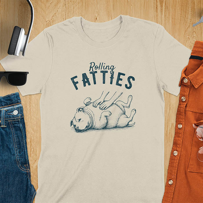 Sand colored t-shirt with 'Rolling Fatties' text and illustration of chubby pitbull dog lying on its back with paws up, with human hands on the dog's belly