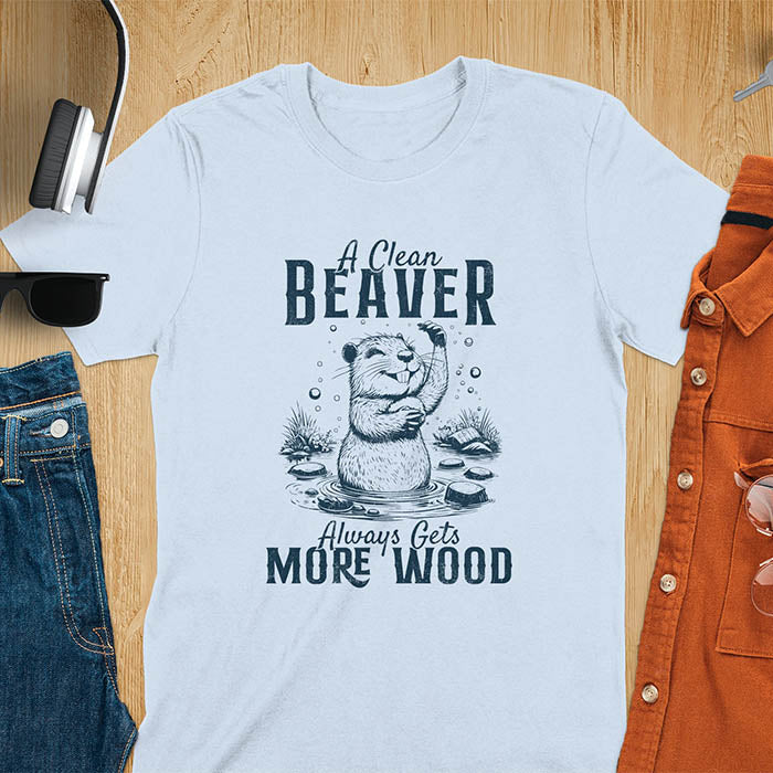Light blue t-shirt featuring illustrated beaver bathing in water with text 'A Clean Beaver Always Gets More Wood' - adult humor meme design with cartoon beaver surrounded by water bubbles and tree stumps