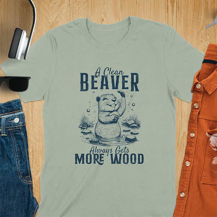 Sage green t-shirt featuring illustrated beaver bathing in water with text 'A Clean Beaver Always Gets More Wood' - adult humor meme design with cartoon beaver surrounded by water bubbles and tree stumps