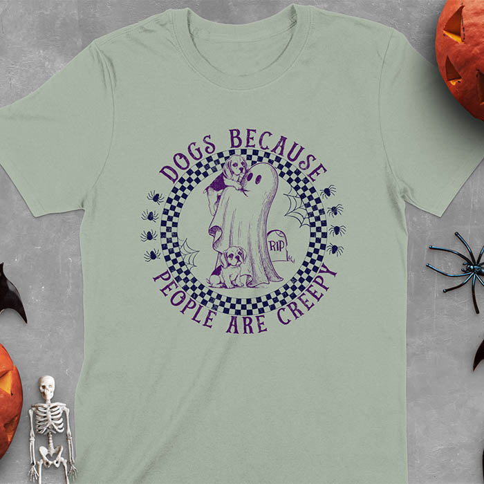 Sage green Halloween t-shirt featuring a cute ghost holding a beagle puppy with another beagle sitting on the ground next to a tombstone marked 'RIP', surrounded by spiders in a circular checkered border design with text 'DOGS BECAUSE PEOPLE ARE CREEPY'