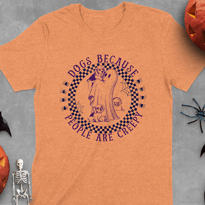 Heather Orange Halloween t-shirt featuring a cute ghost holding a beagle puppy with another beagle sitting on the ground next to a tombstone marked 'RIP', surrounded by spiders in a circular checkered border design with text 'DOGS BECAUSE PEOPLE ARE CREEPY'