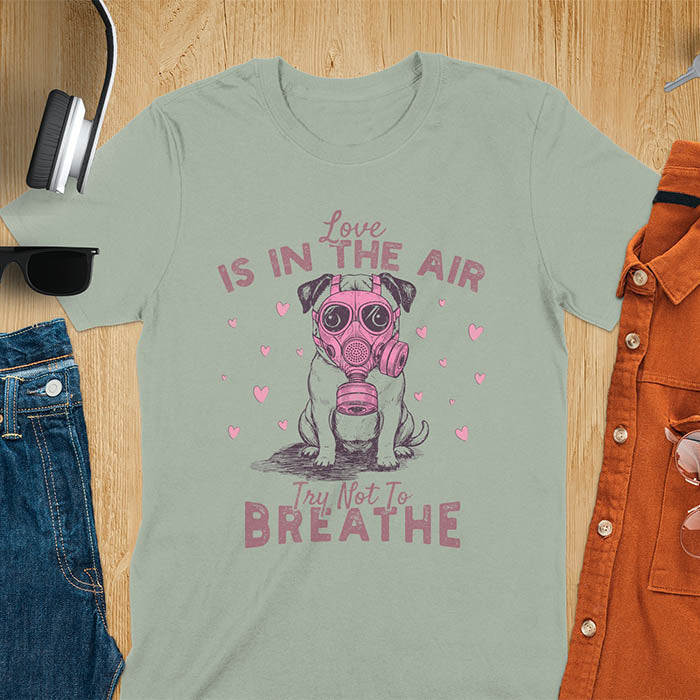 Anti-Valentine's Day pug wearing pink gas mask graphic tee with Love is in the Air Try Not to Breathe text and hearts on sage green shirt