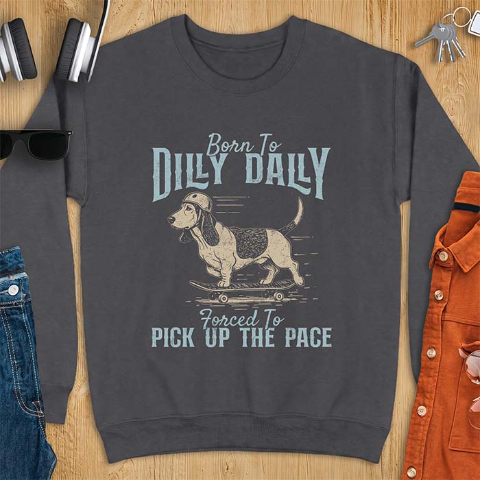 Dark Heather sweatshirt with a graphic of a basset hound in a skater helmet riding a skateboard with long ears flying back, printed with the text Born To Dilly Dally, Forced To Pick Up The Pace