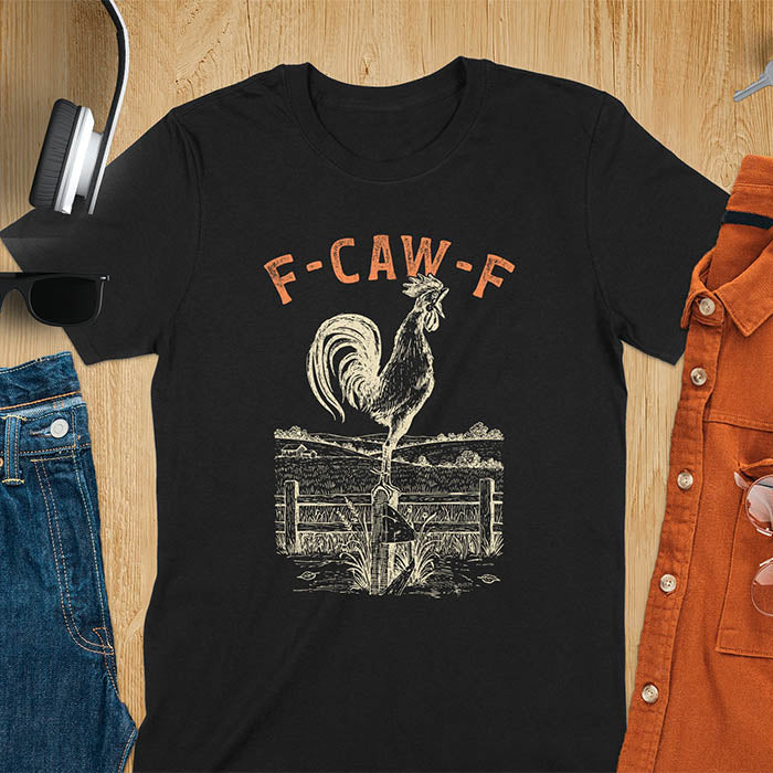 Black t-shirt with F-CAW-F text and detailed rooster illustration standing on wooden fence in vintage farm scene style