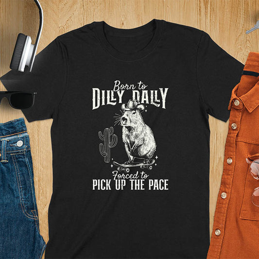 A black color t-shirt featuring a Capybara in a cowboy hat on a skateboard western style. Born to Dilly Dally and Forced to Pick Up the Pace text. Distressed style.