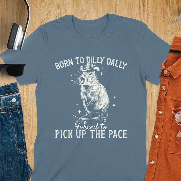 Indigo blue color tee featuring a Capybara in a cowboy hat on a skateboard. Born to Dilly Dally and Forced to Pick Up the Pace text. Distressed style.