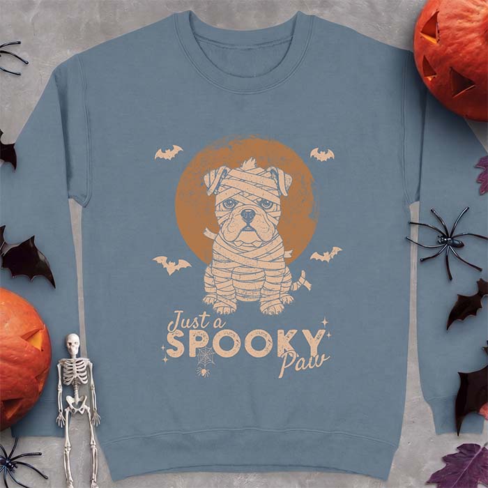 Indigo Blue sweatshirt with a Halloween graphic of an English Bulldog puppy wrapped as a mummy sitting in front of a full moon with bats and a spider web, and the text Just A Spooky Paw