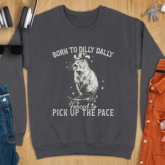 Dark Heather sweatshirt with a graphic of a capybara wearing a cowboy hat riding a skateboard surrounded by sparkles, with the text Born To Dilly Dally Forced To Pick Up The Pace