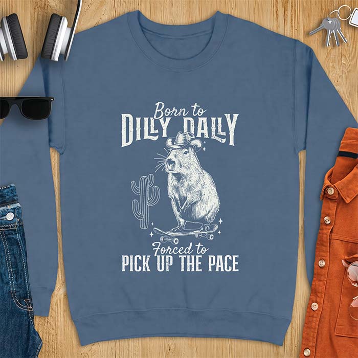 Indigo Blue sweatshirt with a graphic of a capybara wearing a cowboy hat balanced on a skateboard beside a cactus, plus the text Born to Dilly Dally and Forced to Pick Up The Pace.