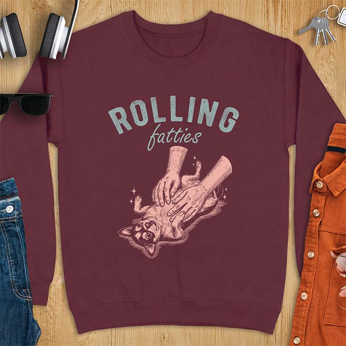 Maroon sweatshirt with a graphic of a chubby Chihuahua rolled onto its back getting a two-handed belly rub with tiny sparkles around it, above the text Rolling Fatties