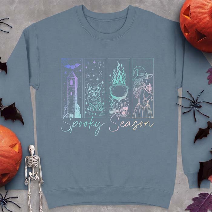 Indigo Blue sweatshirt with a four-panel Halloween graphic of a haunted tower, a bandage-wrapped Corgi mummy, a bubbling cauldron with potion bottles and a witch holding flowers, with the text Spooky Season