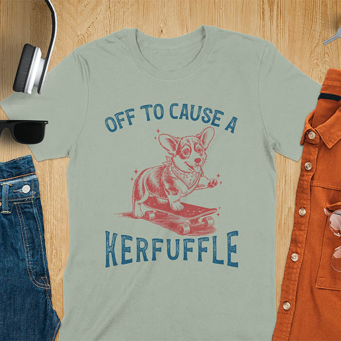 Sage green t-shirt with Off To Cause A Kerfuffle text and cute corgi puppy attempting skateboarding illustration