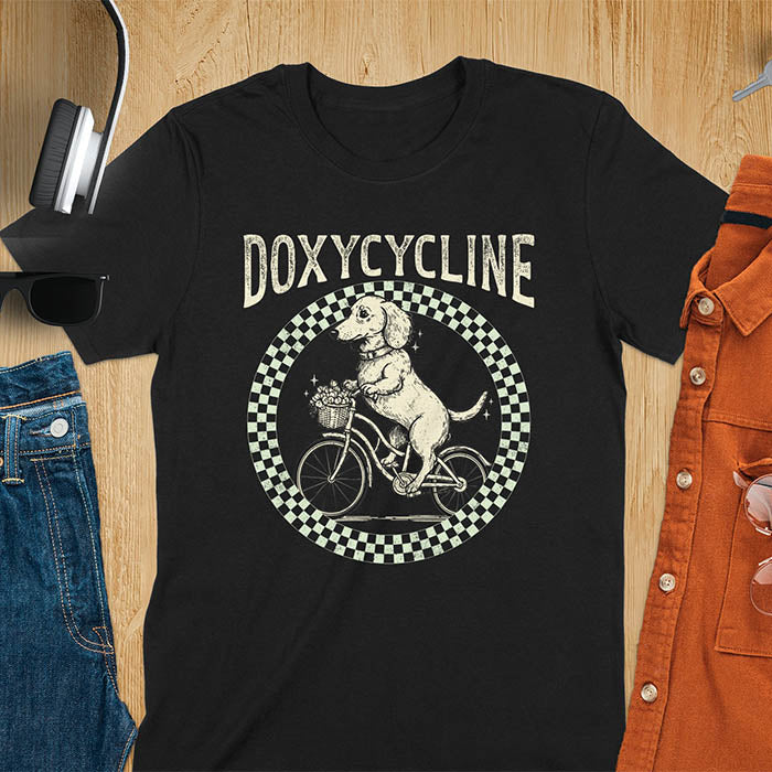 Black Dachshund t-shirt with 'DOXYCYCLINE' text and cute wiener dog riding bicycle in checkered circle design