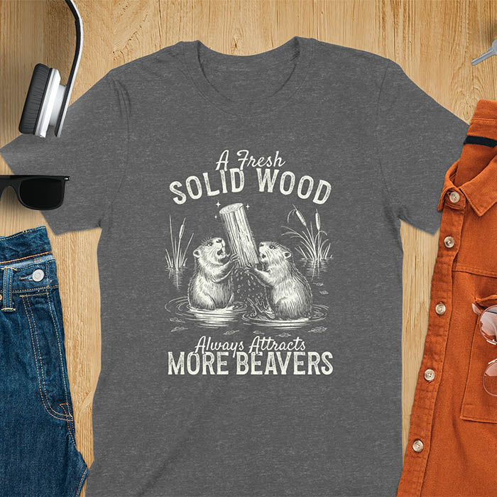 Dark heather t-shirt with vintage-style illustration of two beavers in water fighting over a wooden log, featuring text 'A Fresh Solid Wood Always Attracts More Beavers' in rustic lettering