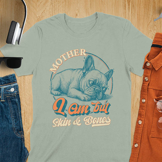 French Bulldog lying down with a sulky expression, with the text Mother I Am But Skin and Bones in retro typography on a sage green t-shirt