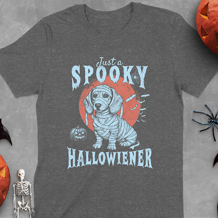 Dark Heather t-shirt featuring a cute dachshund puppy wrapped in mummy bandages with text 'Just a Spooky Hallowiener', jack-o'-lantern pumpkin, red moon and flying bats in background