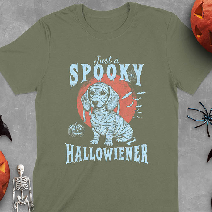 Military Green t-shirt featuring a cute dachshund puppy wrapped in mummy bandages with text 'Just a Spooky Hallowiener', jack-o'-lantern pumpkin, red moon and flying bats in background