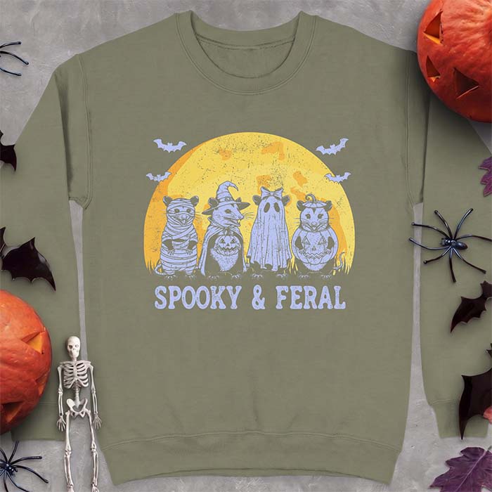 Military Green sweatshirt with a Halloween graphic of four opossums dressed as a mummy, a witch, a ghost and a pumpkin standing under a glowing moon with bats and the text Spooky & Feral