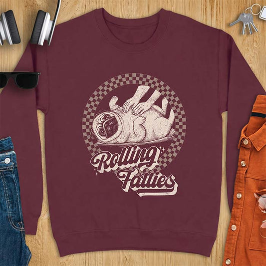 Maroon sweatshirt with a graphic of a pug lying on its back inside a checkered circle while a pair of hands press into its rolled folds and the text Rolling Fatties
