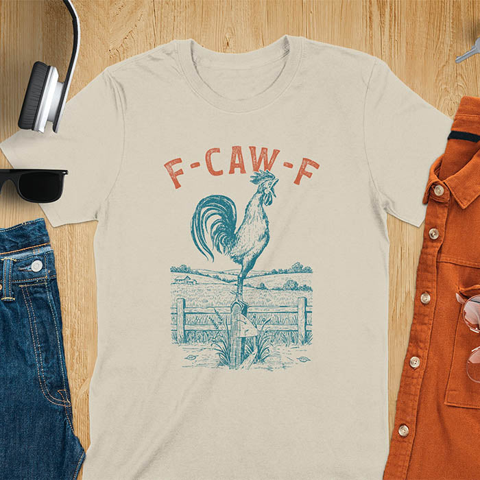 Sand color t-shirt with F-CAW-F text and detailed rooster illustration standing on wooden fence in vintage farm scene style