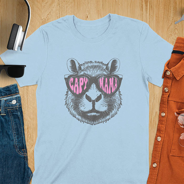 A t-shirt featuring a capybara face with pink heart-shaped sunglasses that spell CAPY MAMA. Below the capybara, Meagan is written in a pink, script font. This vintage mama shirt design is a retro mom tee-shirt perfect for mama mom life. A trendy mama tee for an expecting mom or pregnant mom gift, ideal for a pregnancy announce or pregnancy reveal. A great mom gift hers or mother days gift, or a new mom gift for a gift for wife. Personalization is available by changing the Meagan name.