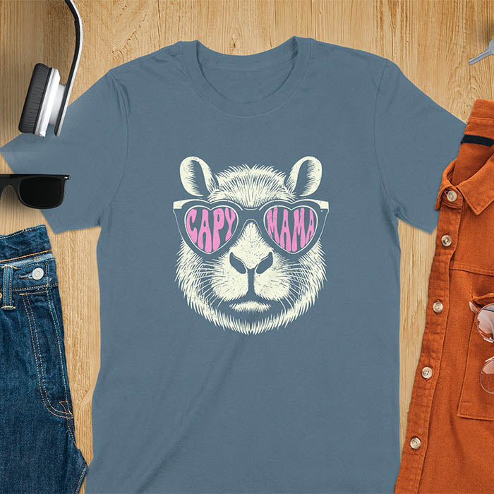 A t-shirt featuring a capybara face with pink heart-shaped sunglasses that spell CAPY MAMA. Below the capybara, Meagan is written in a pink, script font. This vintage mama shirt design is a retro mom tee-shirt perfect for mama mom life. A trendy mama tee for an expecting mom or pregnant mom gift, ideal for a pregnancy announce or pregnancy reveal. A great mom gift hers or mother days gift, or a new mom gift for a gift for wife. Personalization is available by changing the Meagan name.