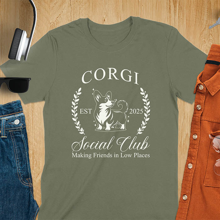 Our charming Corgi Social Club t-shirt features a delightful illustration of a corgi surrounded by laurel branches, with playful text that reads CORGI Social Club and Making friends in low places.