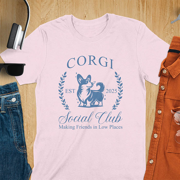 Our charming Corgi Social Club t-shirt features a delightful illustration of a corgi surrounded by laurel branches, with playful text that reads CORGI Social Club and Making friends in low places.