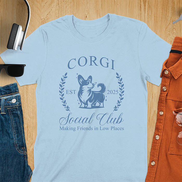 Our charming Corgi Social Club t-shirt features a delightful illustration of a corgi surrounded by laurel branches, with playful text that reads CORGI Social Club and Making friends in low places.