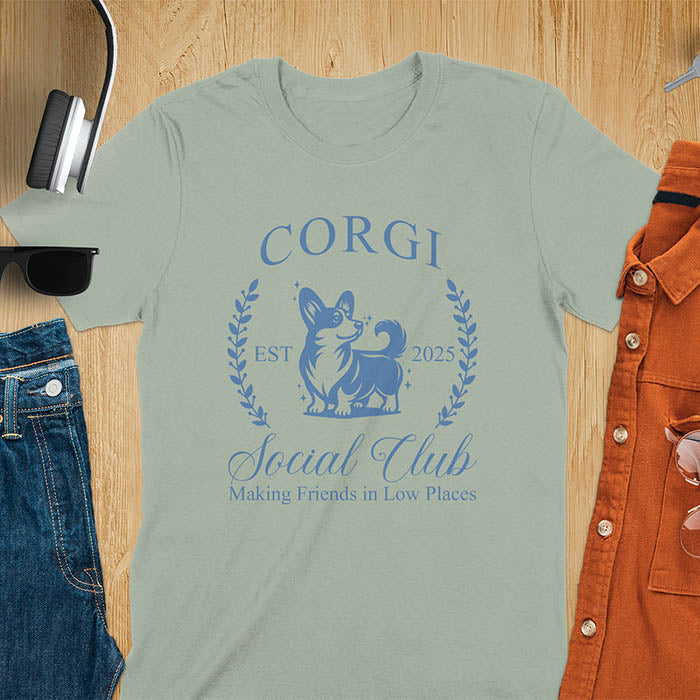 Our charming Corgi Social Club t-shirt features a delightful illustration of a corgi surrounded by laurel branches, with playful text that reads CORGI Social Club and Making friends in low places.