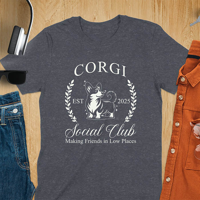 Our charming Corgi Social Club t-shirt features a delightful illustration of a corgi surrounded by laurel branches, with playful text that reads CORGI Social Club and Making friends in low places.