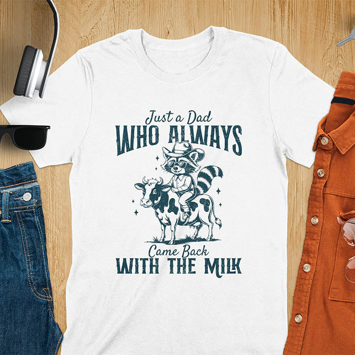 A t-shirt with a raccoon wearing a cowboy hat and sunglasses, riding a cow. Text: Just a Dad WHO ALWAYS above and Came Back WITH THE MILK below. This funny raccoon shirt features funny graphics, a dad t shirt for a funny fathers day or fathers day gift. A funny shirt for dad or gift for dad, a husband gift or father in law gifts. Could be used for a dad announcement, expectant dad, or godfather proposal.