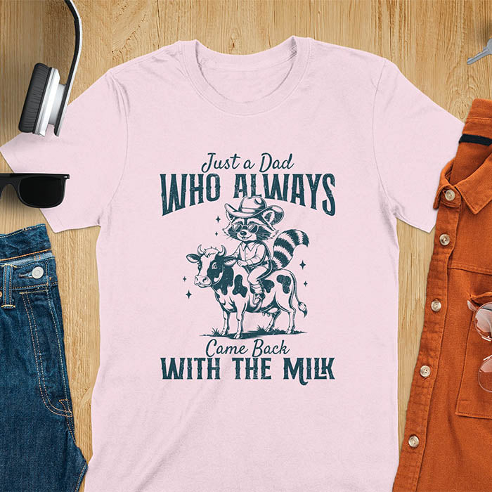 A t-shirt with a raccoon wearing a cowboy hat and sunglasses, riding a cow. Text: Just a Dad WHO ALWAYS above and Came Back WITH THE MILK below. This funny raccoon shirt features funny graphics, a dad t shirt for a funny fathers day or fathers day gift. A funny shirt for dad or gift for dad, a husband gift or father in law gifts. Could be used for a dad announcement, expectant dad, or godfather proposal.