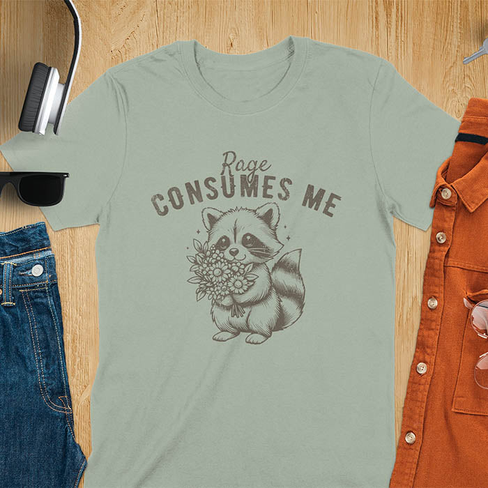 A t-shirt featuring a raccoon holding a bouquet of flowers. Text: Rage CONSUMES ME in a bold, arched font. This dark humor tee is a mental health meme and raccoon meme design. A weirdcore funny and weird funny shirt for a funny gag gift. A raccoon cuteness design, this is one of those shirts that go hard, a unisex and comfortable trendy tee. An animal person gift or girlfriend friend gift, a mom gift alternative.