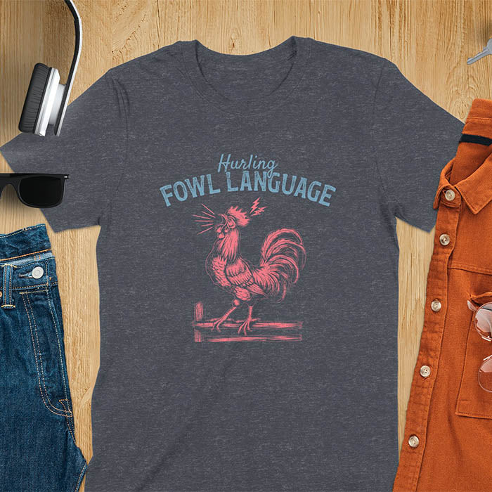 Vintage t-shirt with line art drawing of a chicken rooster standing on a fence in a farm crowing with exaggerated open beak. The design gives a fun and quirky vibe. Text says hurling fowl language.