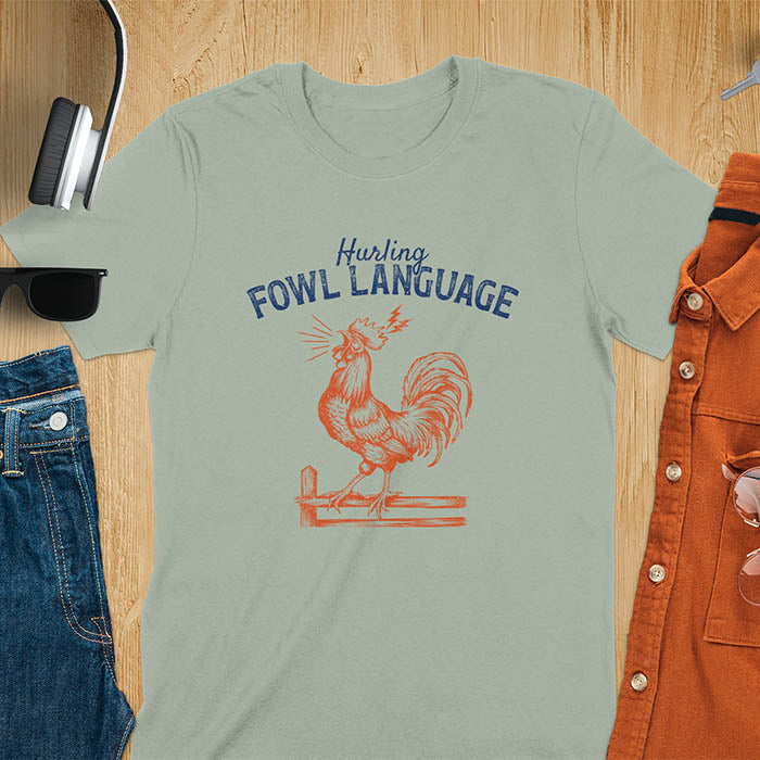 Vintage t-shirt with line art drawing of a chicken rooster standing on a fence in a farm crowing with exaggerated open beak. The design gives a fun and quirky vibe. Text says hurling fowl language.