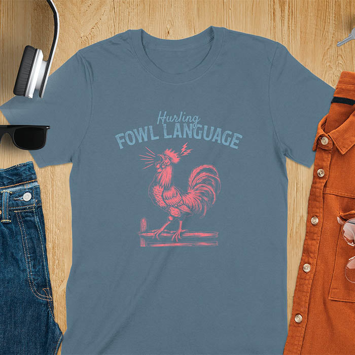 Vintage t-shirt with line art drawing of a chicken rooster standing on a fence in a farm crowing with exaggerated open beak. The design gives a fun and quirky vibe. Text says hurling fowl language.