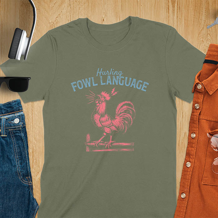 Vintage t-shirt with line art drawing of a chicken rooster standing on a fence in a farm crowing with exaggerated open beak. The design gives a fun and quirky vibe. Text says hurling fowl language.